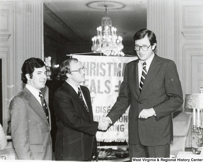 Senator Jay Rockefeller shaking the hand of a unidentified man at the American Lung Disease's Christmas seal event.  Congressman Nick Rahall II is standing beside the unidentified man.