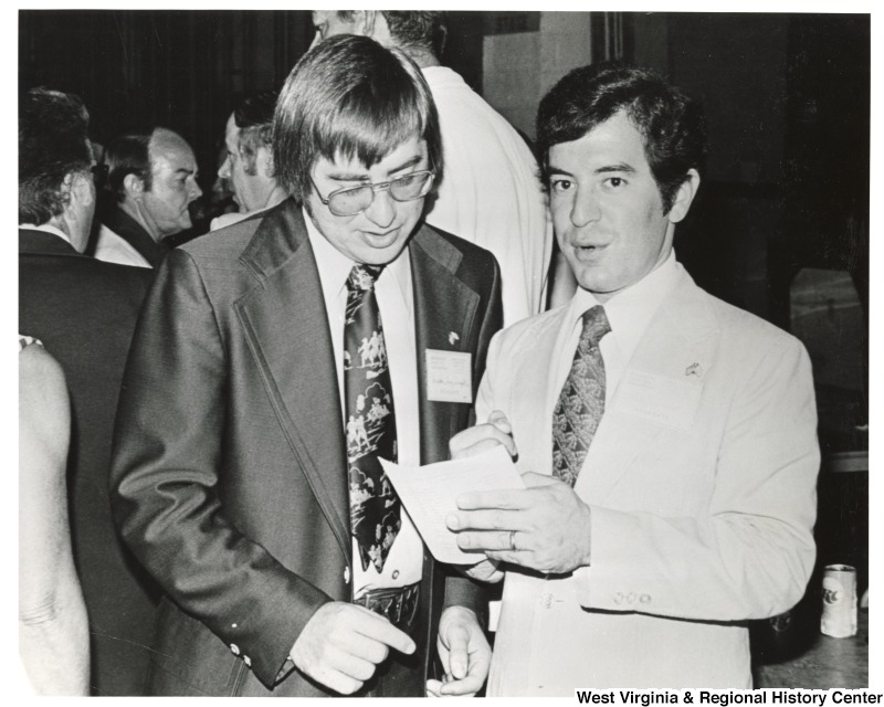 Congressman Nick Rahall II speaking to an unidentified man. Rahall is holding a document which the unidentified man is looking at.