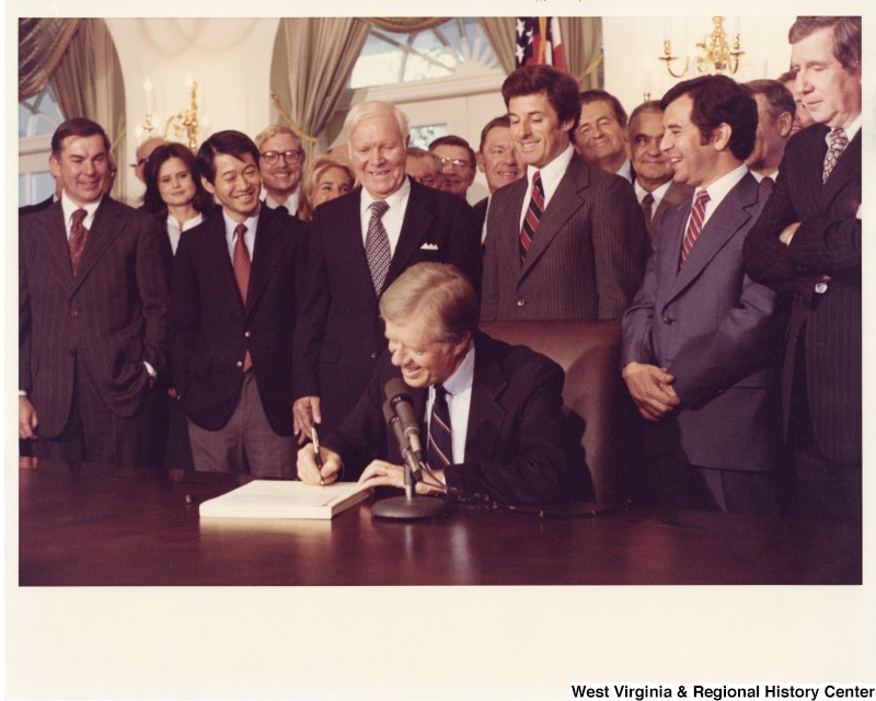 From left to right: Congressman Bob Matsui (D-CA); Congressman Harley Staggers (D-WV); Congressman Jim Florio (D-NJ); Congressman Nick Rahall (D-WV); and former Congressman Fred Rooney (D-PA) who was with the American Association of Railroads. The congressmen are watching President Jimmy Carter sign the railroad deregulation bill (Staggers Rail Act of 1980).