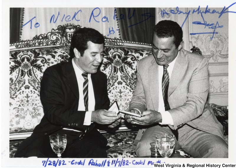 Congressman Nick Rahall II sitting on a couch with Hosni Mubarak. Rahall is showing Mubarak an unidentified item. The photograph is signed: "To Nick Rahall. Sayed Mubarak." The bottom of the photograph states 7/28/1982 Codel Rahall and 11/07/1982 Codel Murthra.