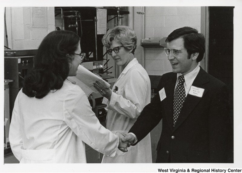 Congressman Nick Rahall II shaking the hand of an unidentified woman who works for Union Carbide. Another unidentified woman is standing right beside them looking at a document.