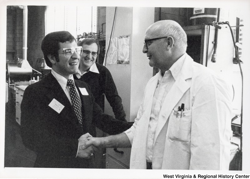 Congressman Nick Rahall II shaking the hand of a unidentified Union Carbide scientist. An unidentified man is standing behind Congressman Rahall.