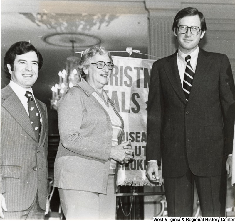 From left to right: Congressman Nick Rahall II, an unidentified woman, and Governor Jay Rockefeller in front of an American Lung Association Christmas Seals banner.