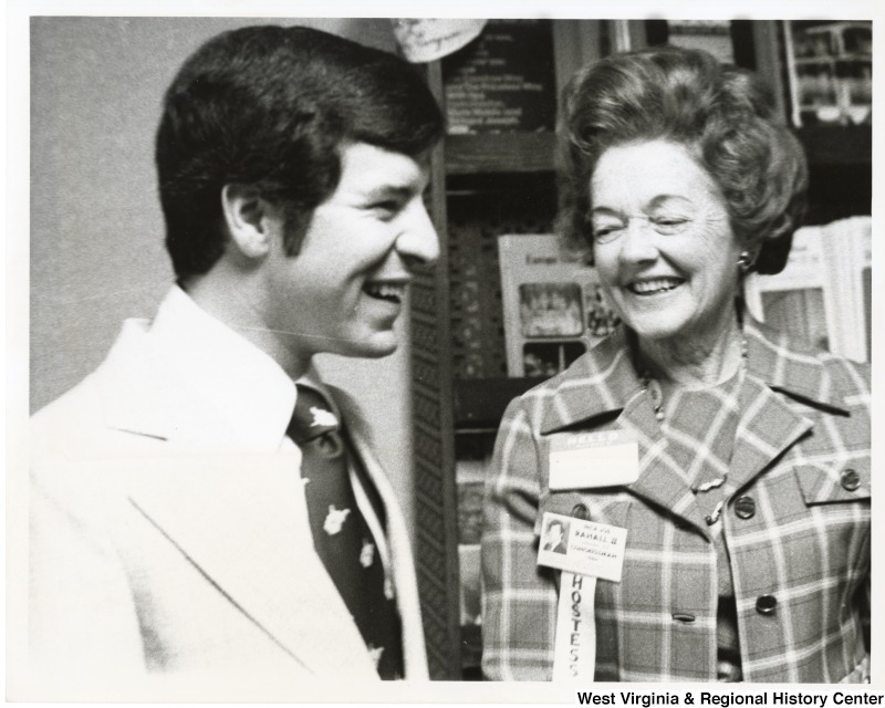 Congressman Nick Rahall II laughing with a unidentified woman wearing a hostess ribbon.