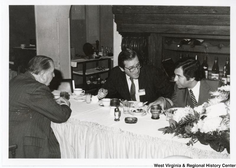 From left to right: Senator Jennings Randolph; Governor John "Jay" Rockefeller; and Congressman Nick Rahall II sitting at a table talking at the 32nd fundraising party at the Democratic Club.