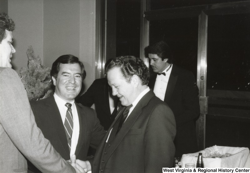 Congressman Nick Rahall II with two unidentified men at one of his birthday parties. The two unidentified men are shaking hands. Two other unidentified men are standing in the background.