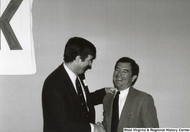 Congressman Nick Rahall II shaking hands with an unidentified man at his birthday party. They are both laughing.