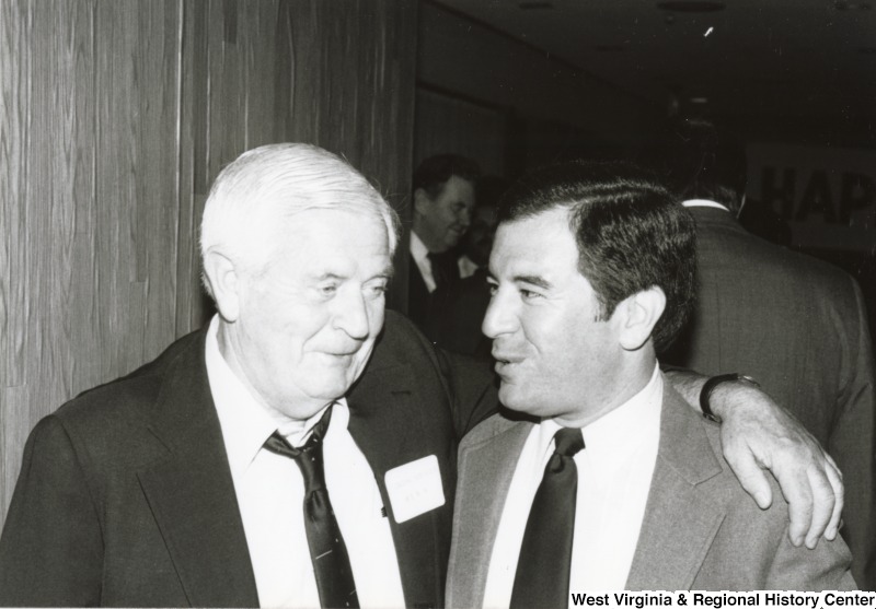 Congressman Nick Rahall II (right) speaking to an unidentified man at his birthday party. The unidentified man has his arm around Rahall's shoulder.