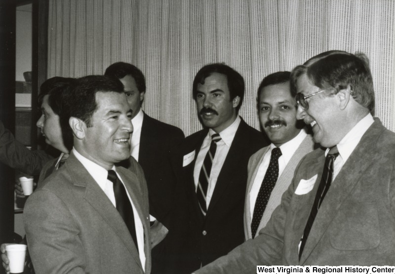 Congressman Nick Rahall II (left) shaking the hand of an unidentified man at his birthday party. Four unidentified men are standing with them.