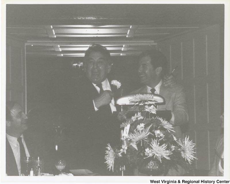 Congressman Nick Rahall II (right) standing and laughing with an unidentified man. The photograph has faded.