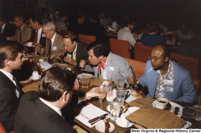 From right to left: S/Sgt. Ezell "Mac" McKinney; Congressman Nick Rahall II; Norman Roberts; Jim Nichols; and two unidentified men at the end. Seated across from Congressman Rahall and Sgt. McKinney are two unidentified men. They are eating at Cattlemen's Steak House in Ft. Worth, Texas.