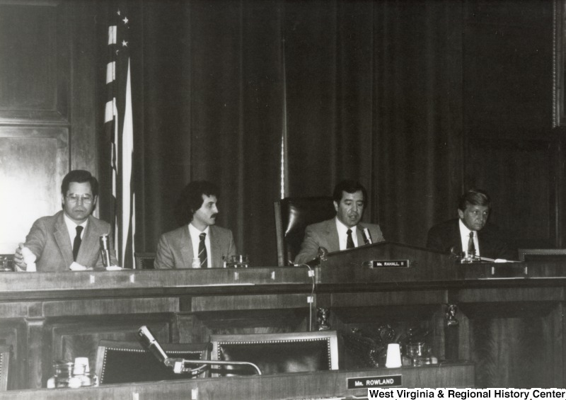 Congressman Nick Rahall II (second from the right) speaking during a committee meeting or hearing. Three unidentified men are seated with him.