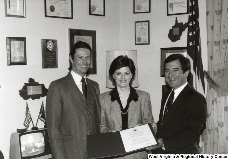 Congressman Nick Rahall II (right) holding a official document with an unidentified woman in his office. An unidentified man stands beside the woman.