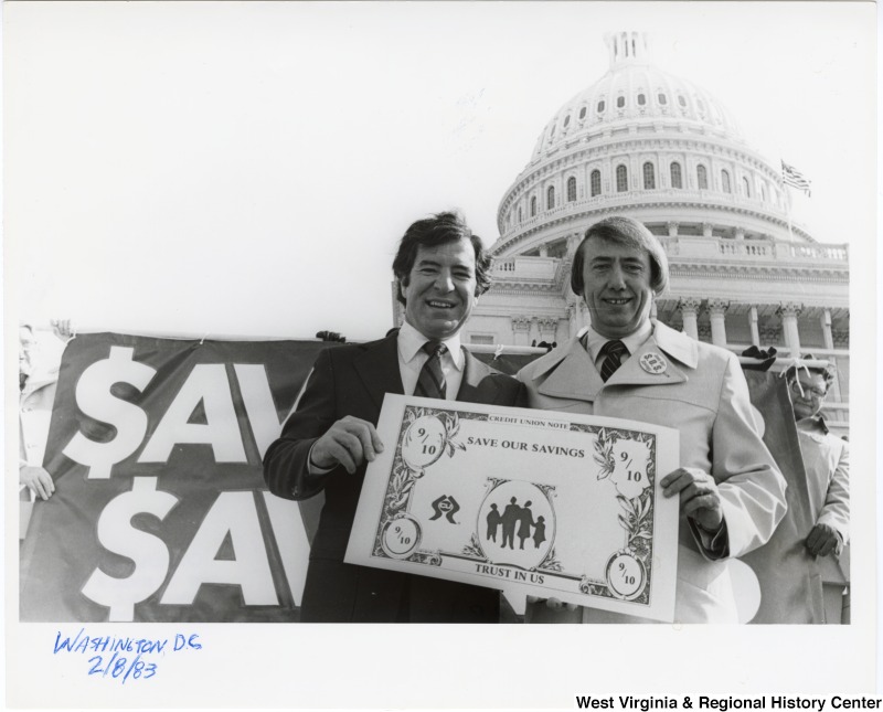 Congressman Nick Rahall, II and an unidentified man in front of the U.S. Capitol building. The two are holding a "Save our Savings" sign.