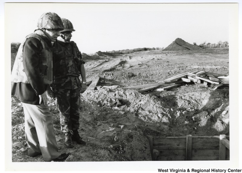 Congressman Nick Rahall, II (left) with an unknown man looking into a military intrenchment in the Middle East.