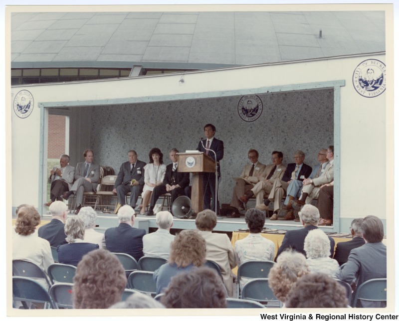 Congressman Nick Rahall, II speaking at the Beckley sewage treatment plant groundbreaking. Senators Jennings Randolph (third from left) and Robert C. Byrd (fifth from left) sit on stage.