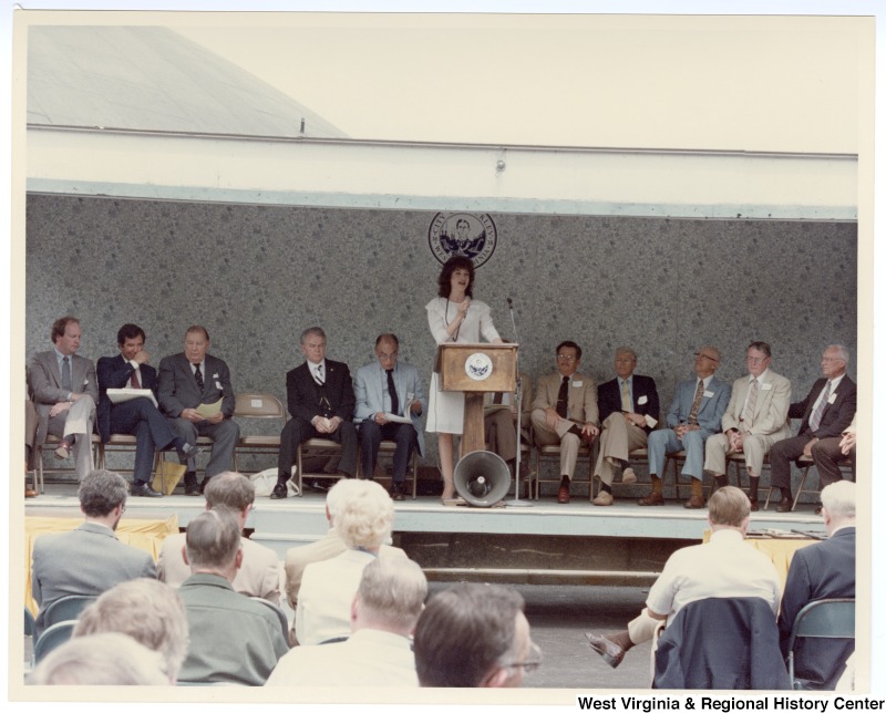 An unidentified woman is speaking the groundbreaking of the Beckley sewage treatment plant. Seated behind her is Congressman Nick Rahall, II (second from left), Senators Jennings Randolph (third from left) and Robert C. Byrd (fourth from left).