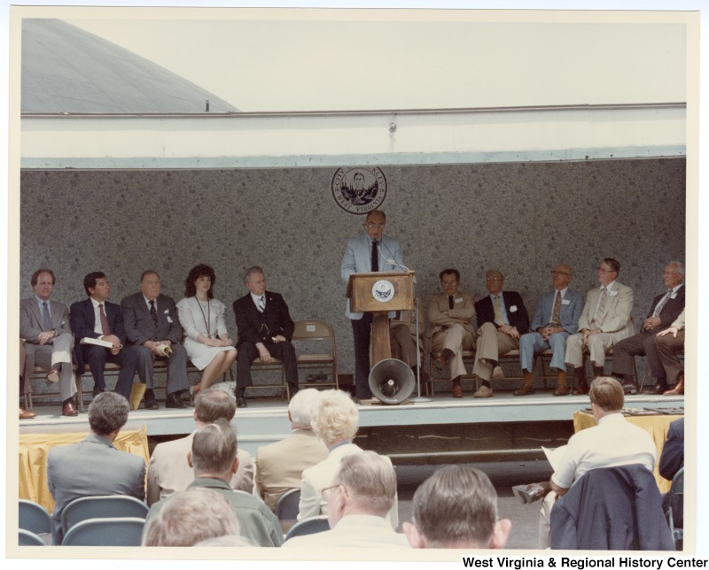 An unidentified man speaking at the groundbreaking for the Beckley sewage treatment plant. Seated behind the unidentified man is Congressman Nick Rahall, II (second from left) and Senators Jennings Randolph (third from left) and Robert C. Byrd (fifth from left).
