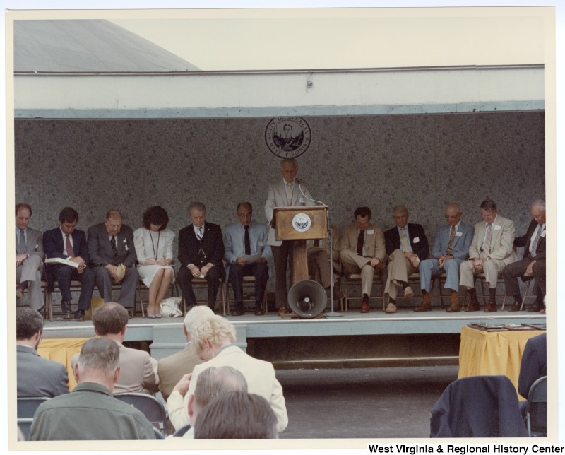 An unidentified man speaking at the groundbreaking for the Beckley sewage treatment plant. Seated behind the unidentified man is Congressman Nick Rahall, II (second from left) and Senators Jennings Randolph (third from left) and Robert C. Byrd (fifth from left).