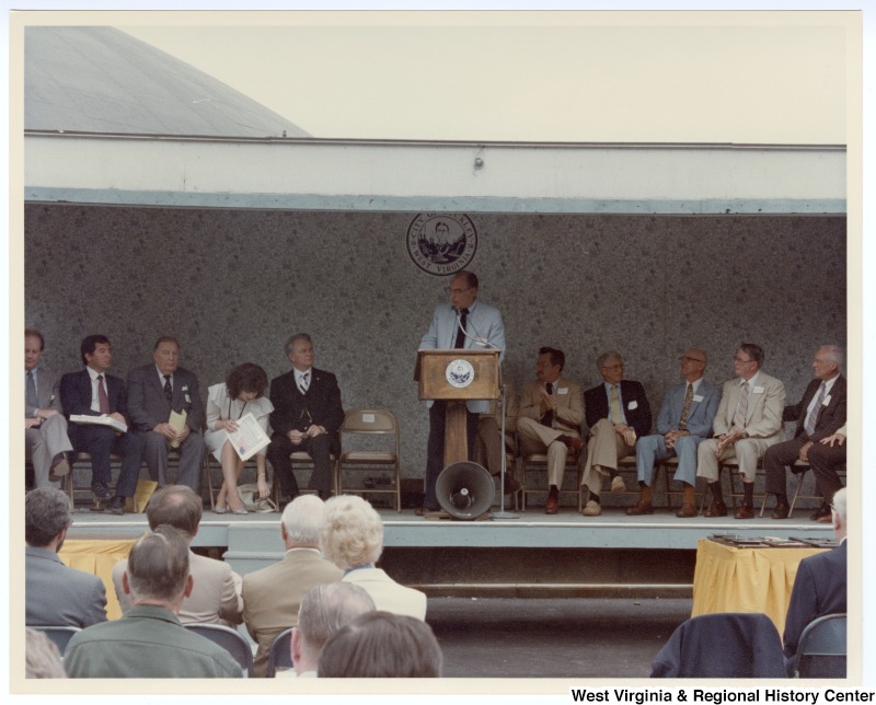 An unidentified man speaking at the groundbreaking for the Beckley sewage treatment plant. Seated behind the unidentified man is Congressman Nick Rahall, II (second from left) and Senators Jennings Randolph (third from left) and Robert C. Byrd (fifth from left).