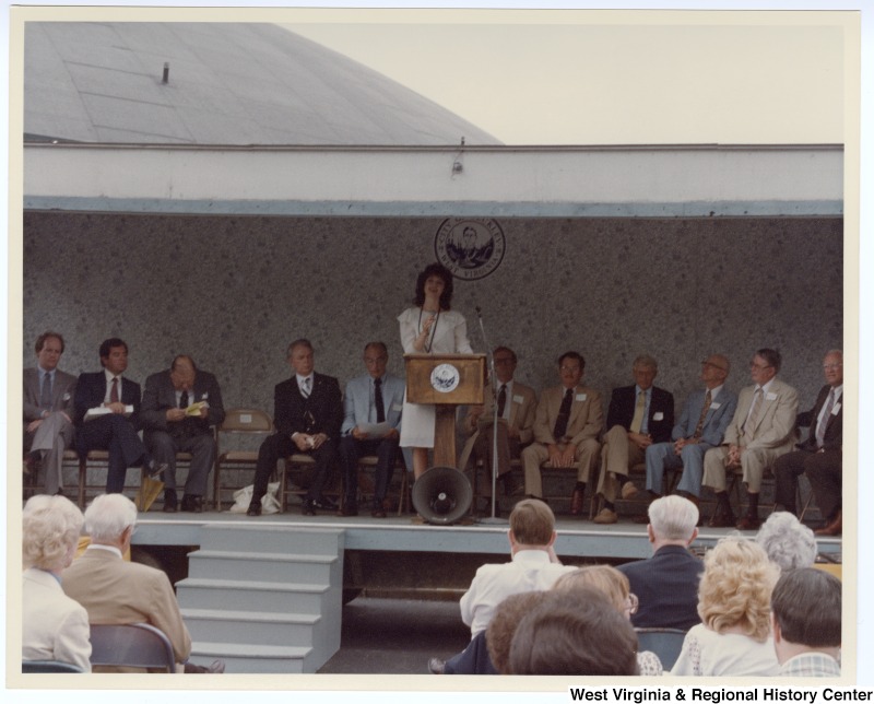 An unidentified woman speaking at the groundbreaking for the Beckley sewage treatment plant. Seated behind the unidentified man is Congressman Nick Rahall, II (second from left) and Senators Jennings Randolph (third from left) and Robert C. Byrd (fifth from left).