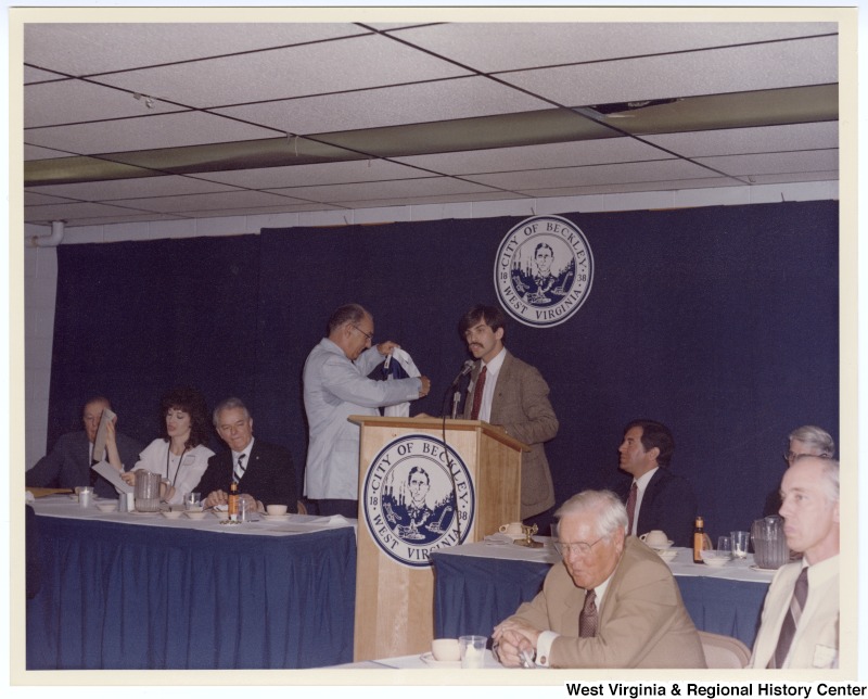 Senators Jennings Randolph (left in back row) and Robert C. Byrd (third from left in back row) as well as Congressman Nick Rahall, II (second from right in back row) at a banquet following the groundbreaking of the Beckley Sewage Treatment plant. An unidentified man holds the West Virginia flag.