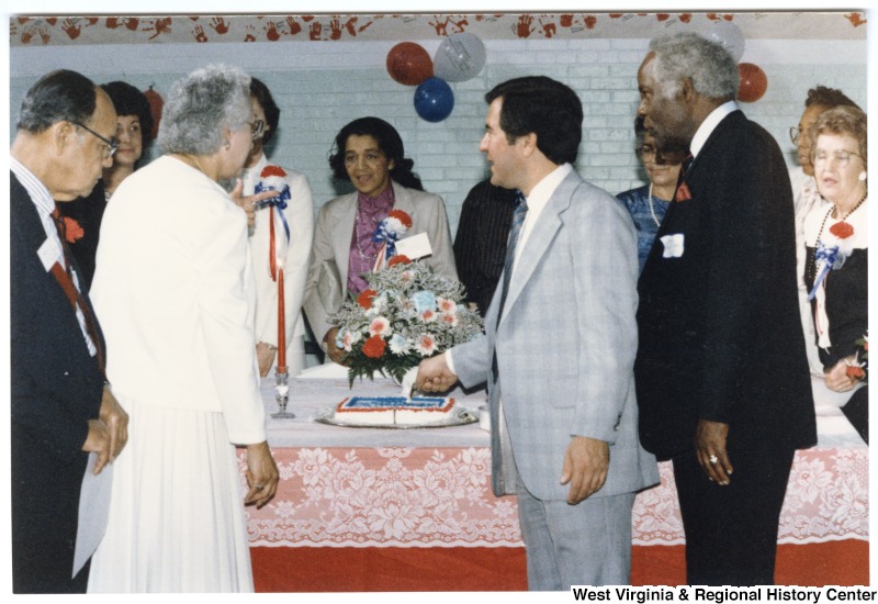 Congressman Nick Rahall, II cutting cake at McDowell County Head Start Program. He is surrounded by unidentified people.The back of the image has written on it: "Lester Toney Bx III Amonate Va. 24601"