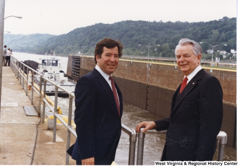 Congressman Nick Rahall, II (left) and Senator Robert C. Byrd (right) in front of a river lock with a boat in it.