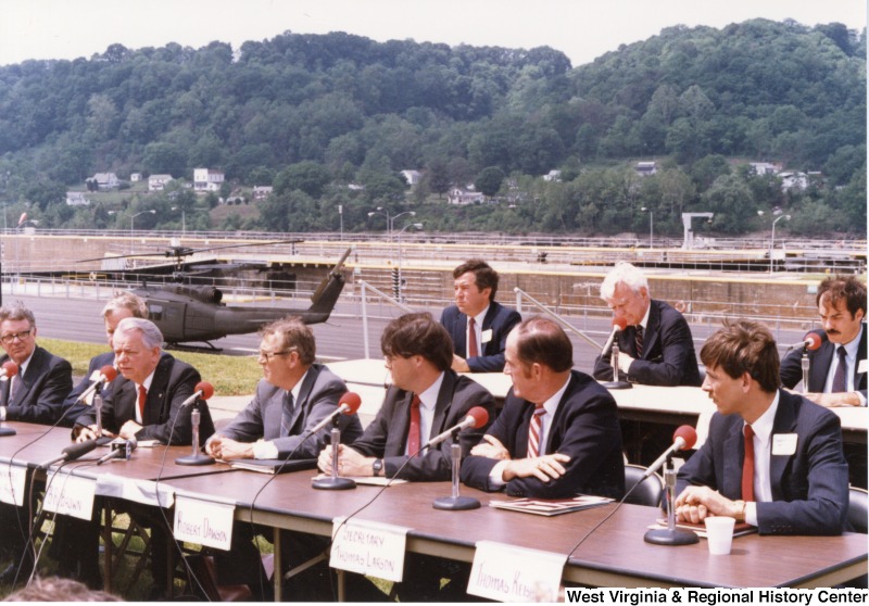 Meeting of men representing governmental agencies and private corporations at a military base. A helicopter is behind the group.From left to right in front row: two unidentified men, Senator Robert C. Byrd (third from left, front row), Consol Energy CEO B. R. "Bobby" Brown, United States Assistant Secretary of the Army Robert Dawson, Pennsylvania Secretary of Transportation Thomas Larson, unidentified man. From left to right in the second row: Congressman Nick Rahall, II, unidentified man, and Congressman Robert "Bob" Wise.