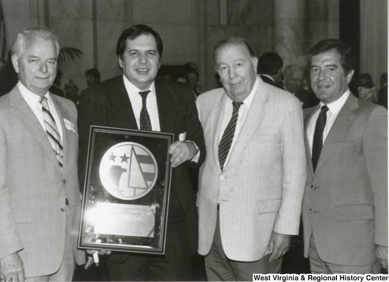 From left to right: Senator Robert C. Byrd, an unidentified man holding a plaque, Senator Jennings Randolph, and Congressman Nick Rahall, II at an event.