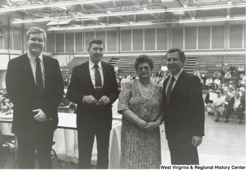 Congressman Nick Rahall, II (left) with two unidentified men and one woman  in front of a basketball court at Marshall University.