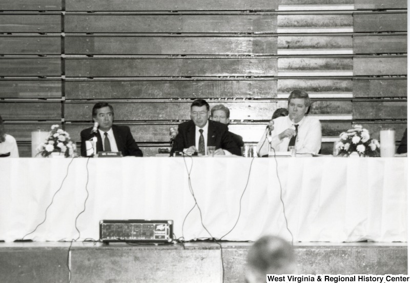 Congressman Nick Rahall, II (left) sitting with two unidentified men at a table on Marshall University's basketball court.