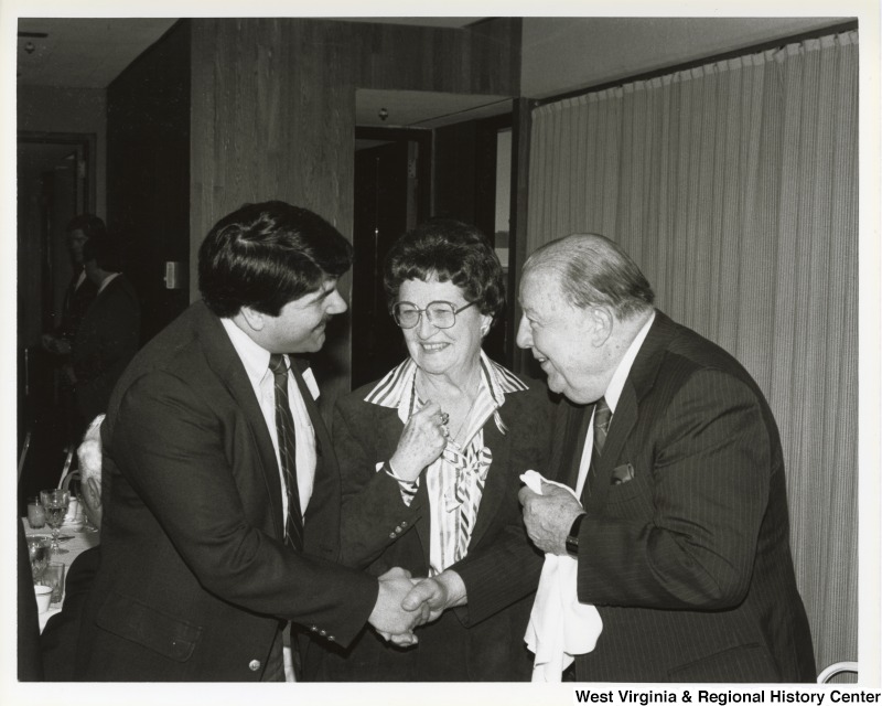 Richard Trumka, president of the United Mine Workers of America (UMWA), shakes hands with Senator Jennings Randolph (D-W.Va.) in front of an unidentified woman at a dinner.
