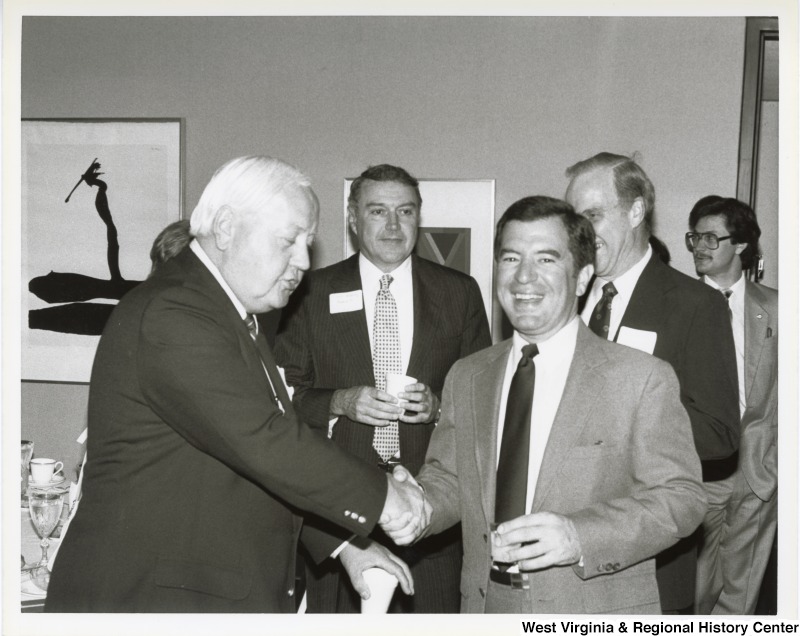 Representative Nick J. Rahall (D-W.Va.) shakes hands with an unidentified man. Standing behind them are three unidentified men.