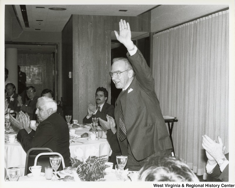 An unidentified man stands waving at a dining event.