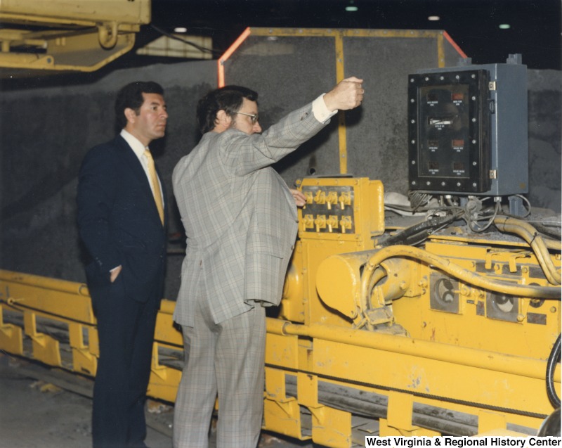 Representative Nick J. Rahall (D-W.Va.) stands next to an unidentified man in front of mining machinery.