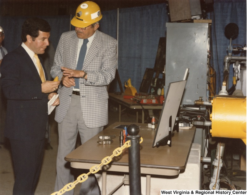Representative Nick J. Rahall (D-W.Va.) speaking to an unidentified man while looking at an array of objects on a desk.
