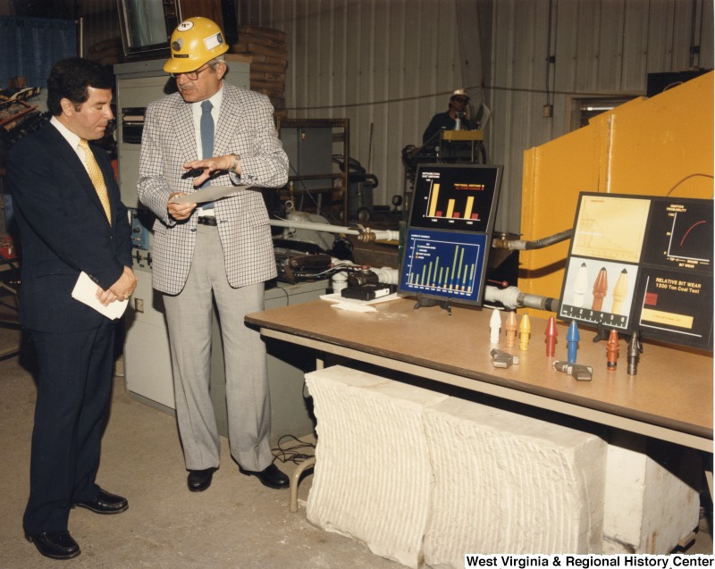 Representative Nick J. Rahall (D-W.Va.) speaking to an unidentified man in front of various displays about coal mining.