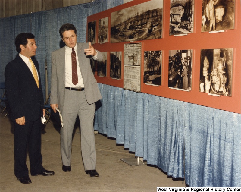 Representative Nick J. Rahall (D-W.Va.) speaking to an unidentified man while looking at historic images of coal mining.