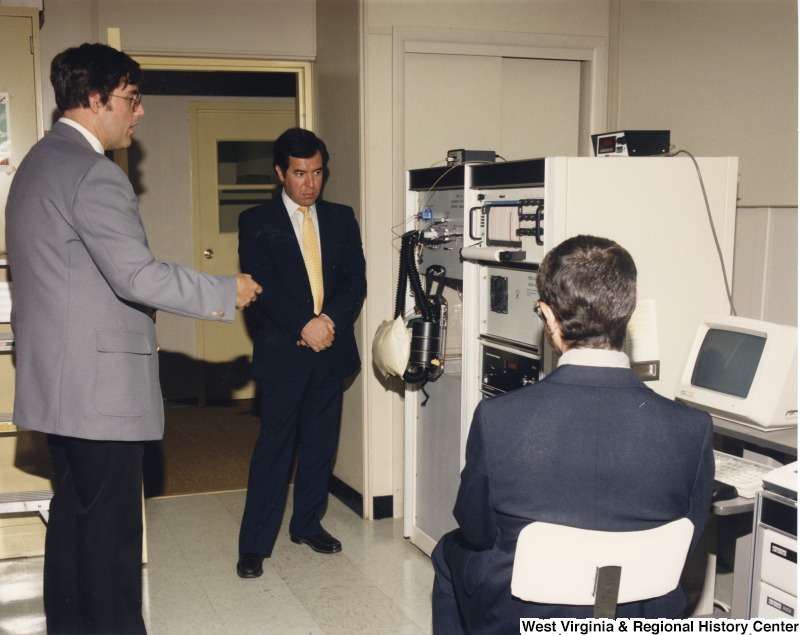 Representative Nick J. Rahall (D-W.Va.) talking with two unidentified men in front of a computer system.