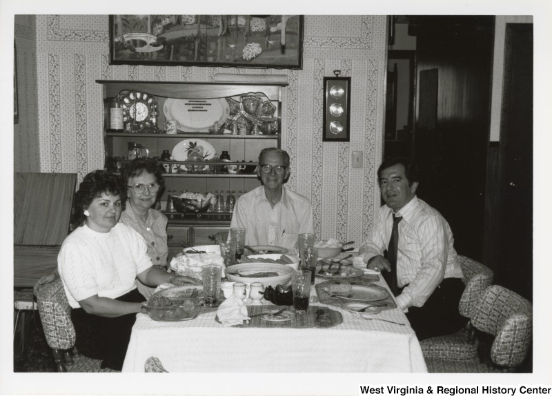 Representative Nick J. Rahall (D-W.Va.) seated on the right side of a full dinner table with an unidentified man at the head and two unidentified women on the left.