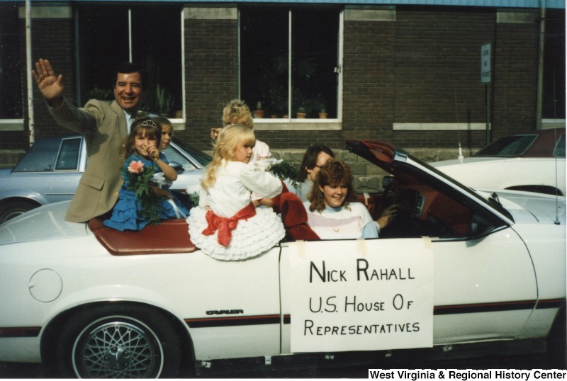 Representative Nick J. Rahall (D-W.Va.) waves from an open car during the Good Bear Parade. Three unidentified children and two unidentified adults ride in the car with him.