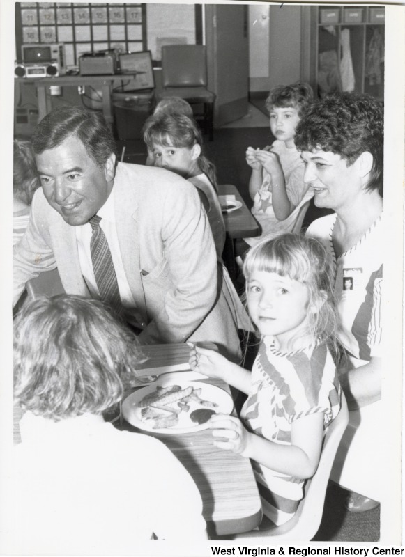Representative Nick J. Rahall (D-W.Va.) seated around a table with several unidentified children and one unidentified woman eating.