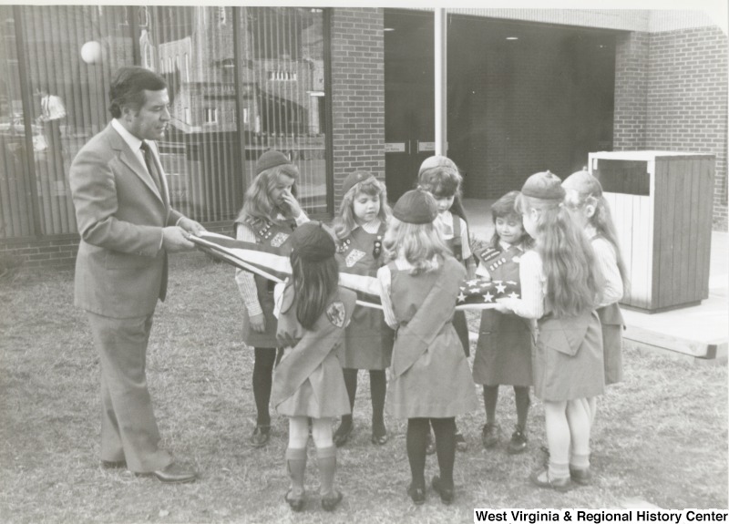 Representative Nick J. Rahall (D-W.Va) helps a group of Girl Scouts fold an American flag.