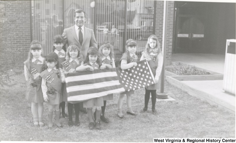 Representative Nick J. Rahall (D-W.Va.) stands behind Girl Scout troop 2540 holding an American flag.