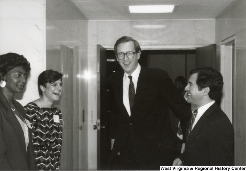 In the center, Senator John D. Rockefeller, IV (D-W.Va.) walks down a hallway with two unidentified women on the left and Representative Nick J. Rahall (D-W.Va.) on the right.