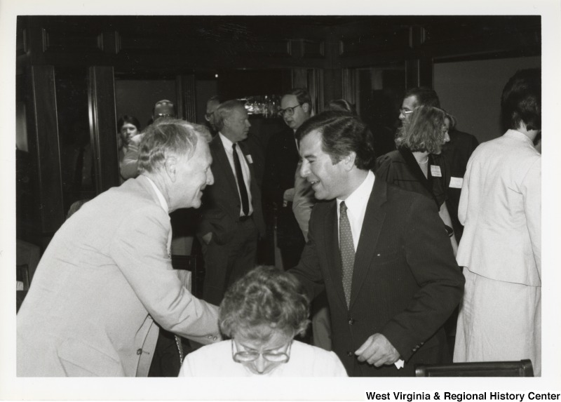 On the right, Representative Nick J. Rahall (D-W.Va.) shakes hands with an unidentified man at an event.