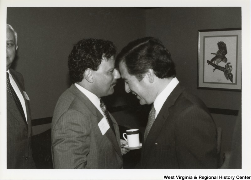 On the right, Representative Nick J. Rahall (D-W.Va.) talks with an unidentified man at an event.