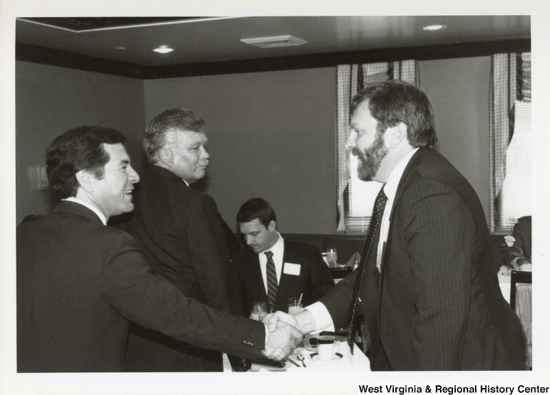 On the left, Representative Nick J. Rahall (D-W.Va.) shakes hands with an unidentified man at an event, with two other unidentified men in the background.