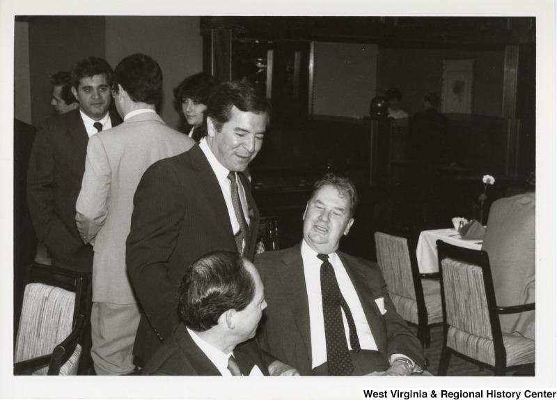Standing, Representative Nick J. Rahall (D-W.Va.) talks with two unidentified men at an event with groups of unidentified people.